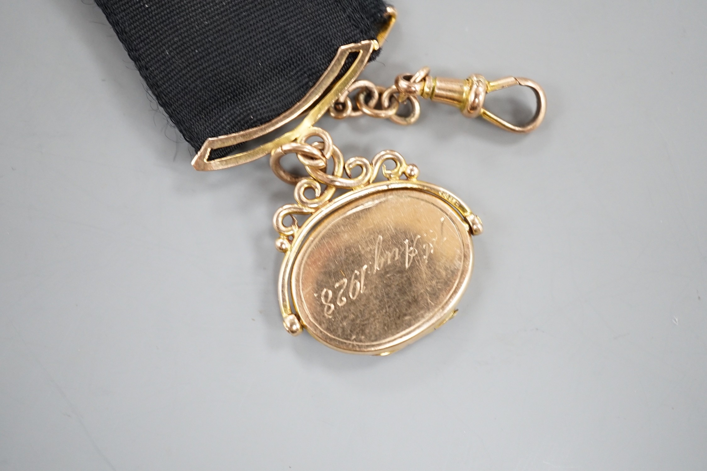 A Victorian yellow metal oval locket fob, hung from a yellow metal mounted black suspension sash, with later engraved date and initials.